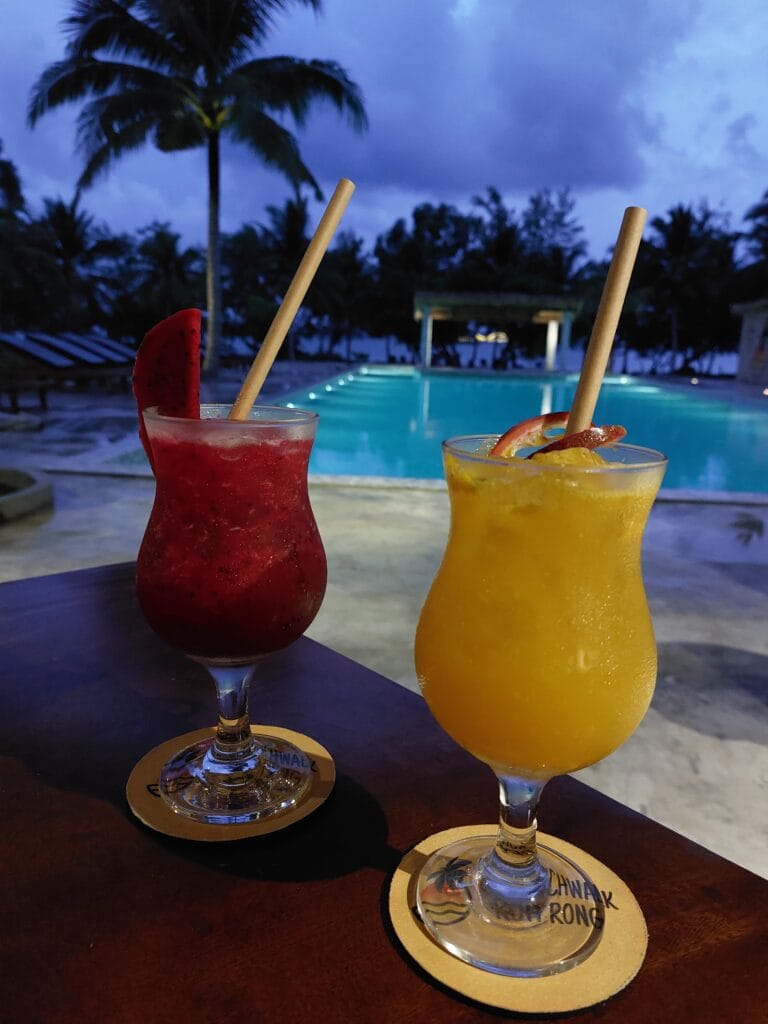 Two cocktails on a table with a beach and a pool in the background