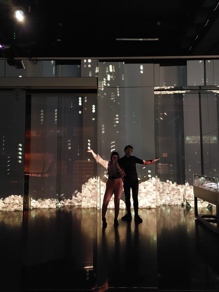 Mirka and Daniel posing in a dark room with coins falling down the wall behind them