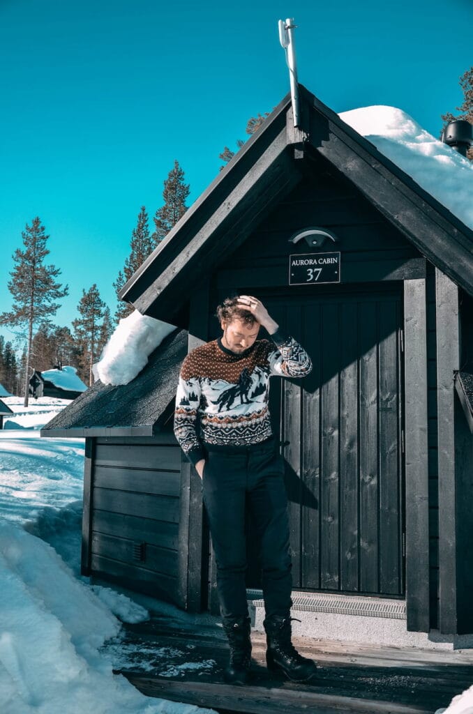 Daniel posing outside of a wooden cabin in a jumper