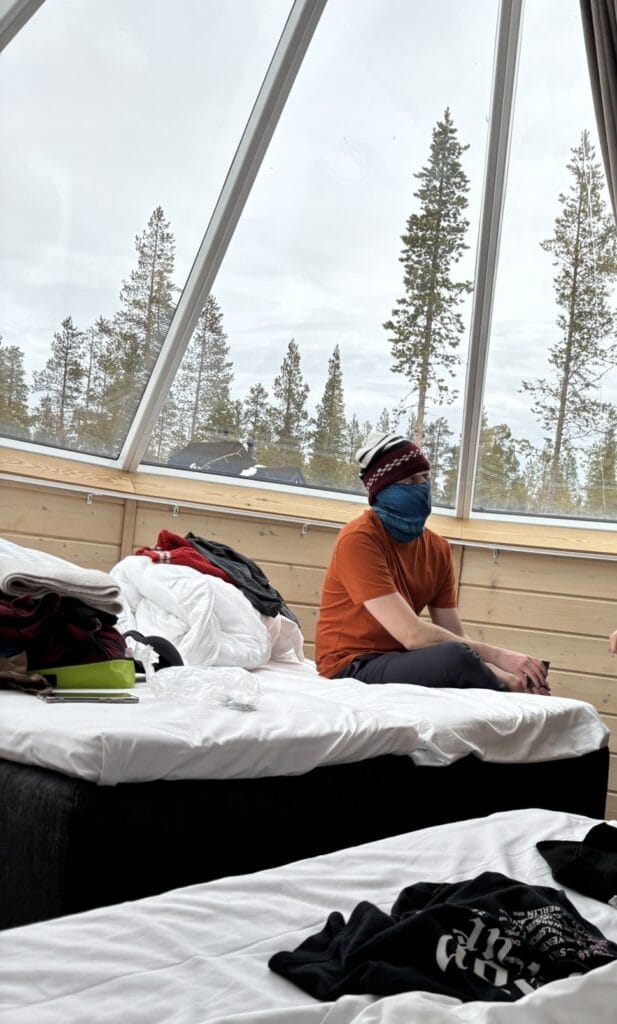 Daniel sitting on a bed with a Buff over his face and a winter hat on