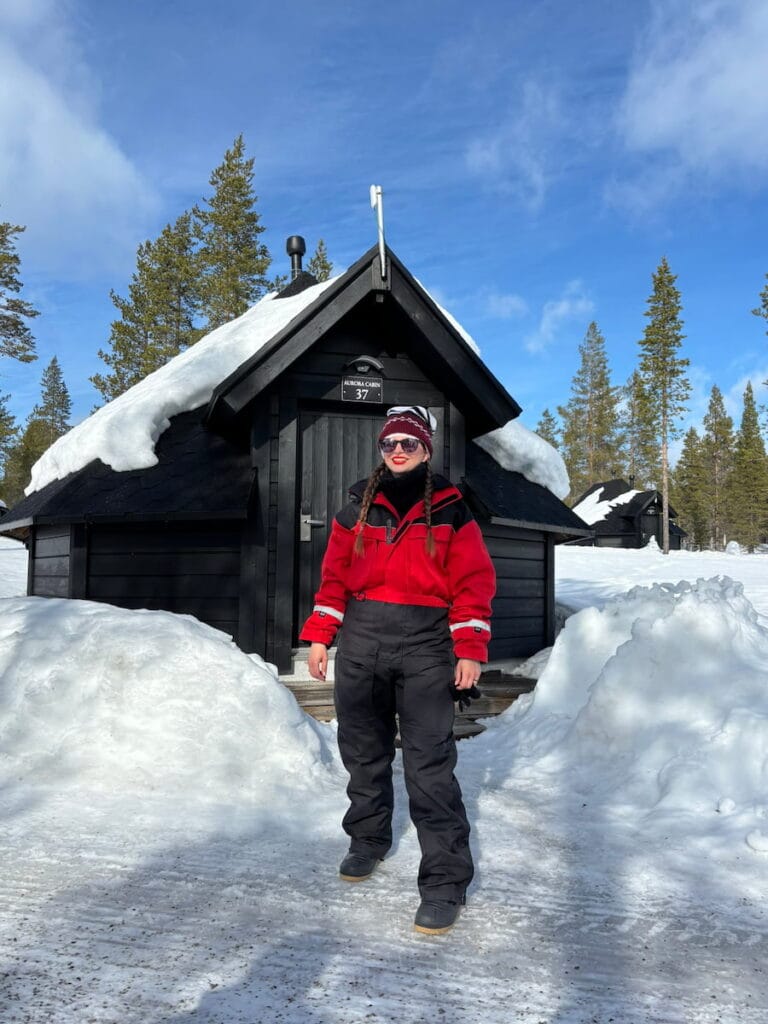 Mirka standing outside of a wooden cabin