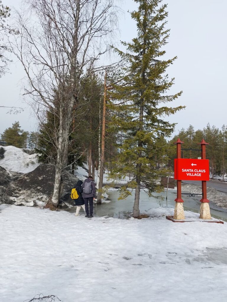 Daniel and Mirka's sister standing at a melting ice pond with a Santa Claus Village sign