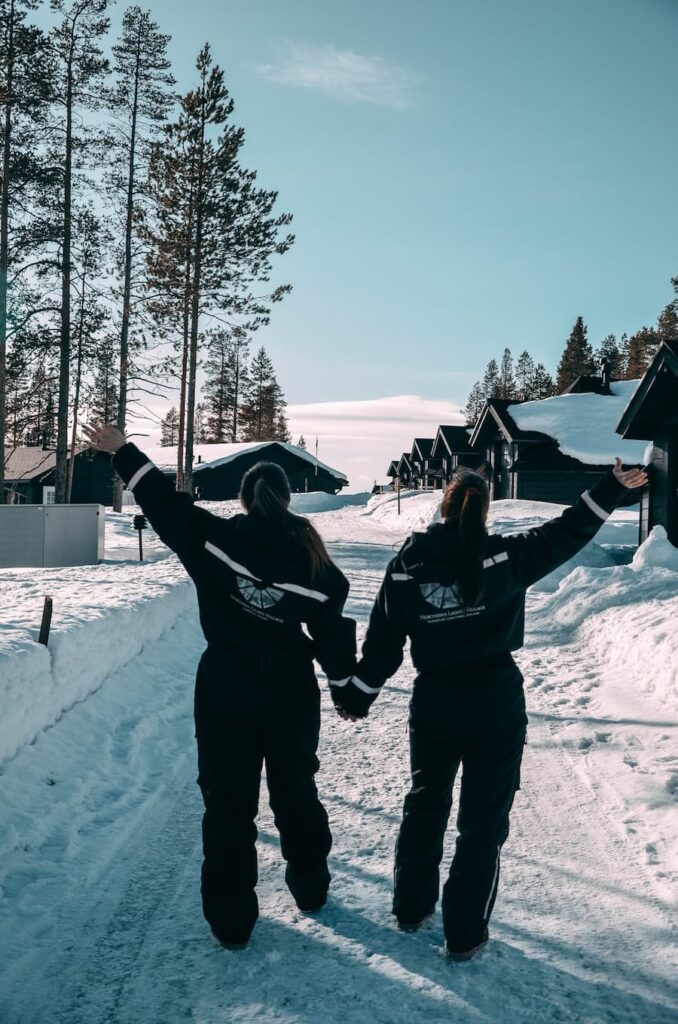 Mirka and Mirka's sister posing in Northern Lights Village snowsuits on a snowy path