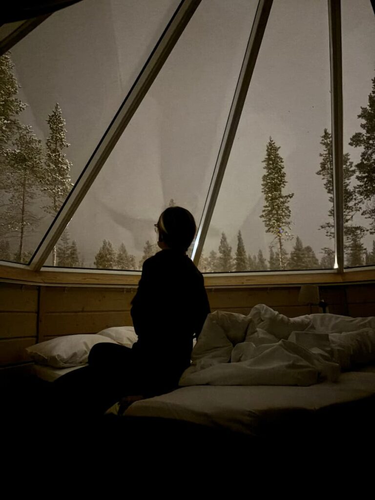 Mirka sitting on a bed in a glass-roof cabin