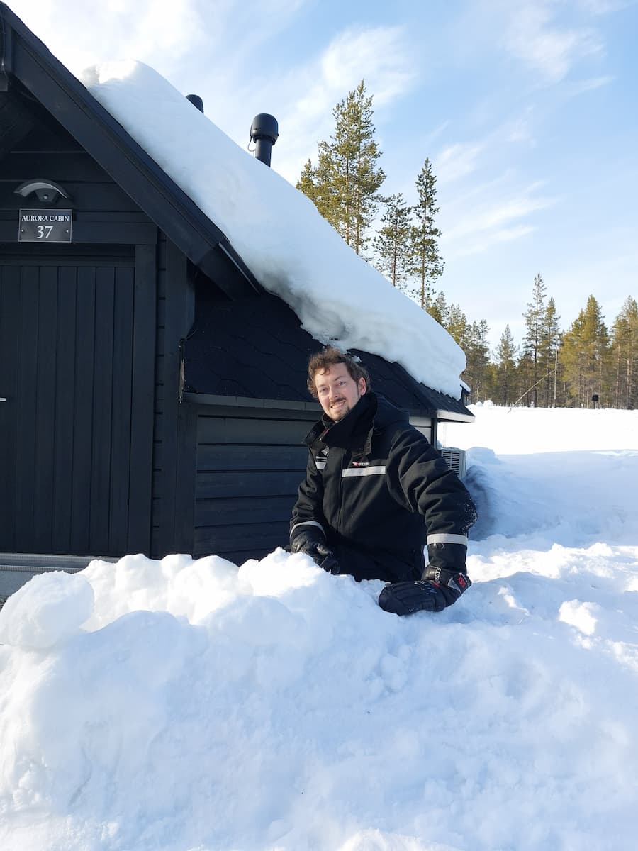 Daniel sitting in the snow outside of an Aurora Cabin